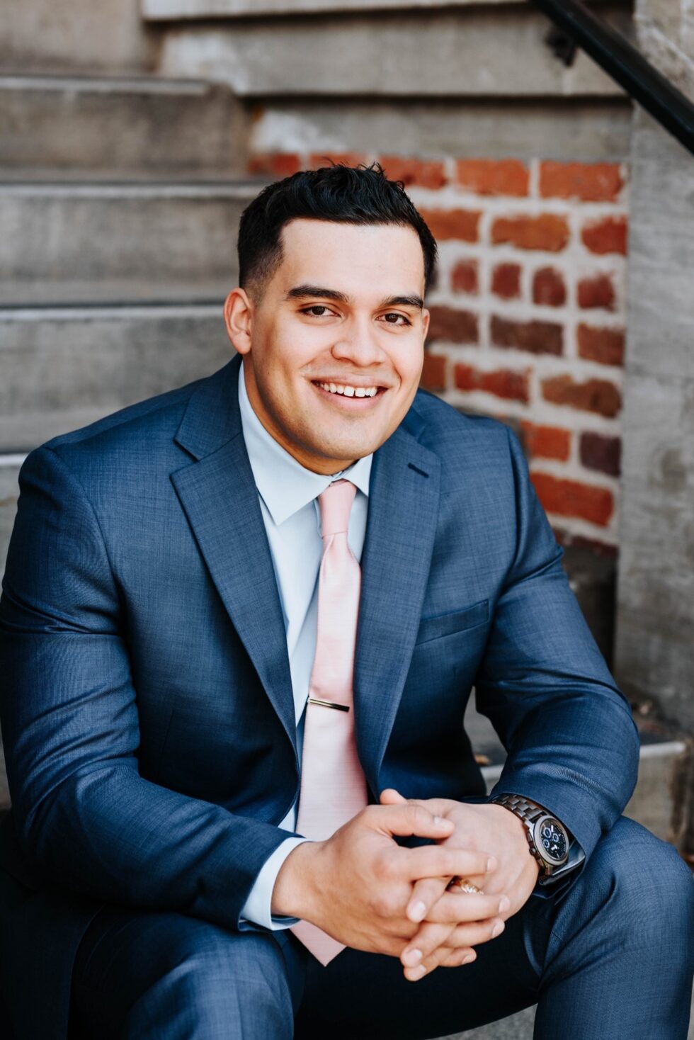 Young man in a suit smiles for camera as he is sitting down.